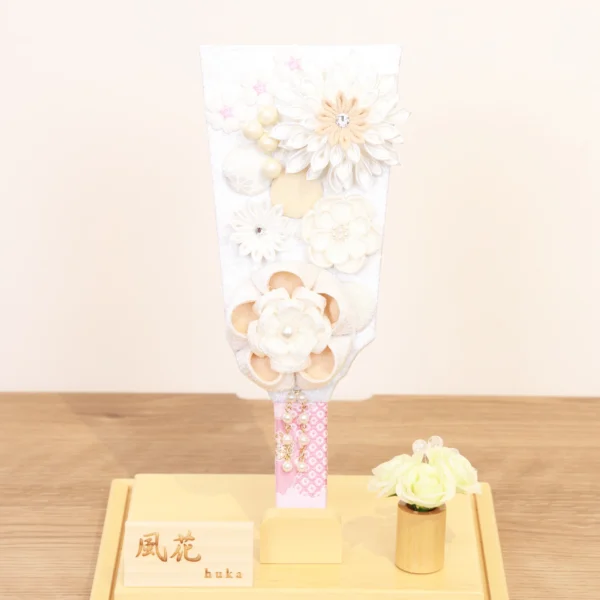 Elegant handcrafted Hagoita paddle adorned with white and beige Kanzashi flowers, set in a wooden base with acrylic case and soft floral accent. Wholesale by Fujikicrafts.