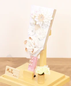 Elegant handcrafted Hagoita paddle adorned with white and beige Kanzashi flowers, set in a wooden base with acrylic case and soft floral accent. Wholesale by Fujikicrafts.