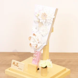 Elegant handcrafted Hagoita paddle adorned with white and beige Kanzashi flowers, set in a wooden base with acrylic case and soft floral accent. Wholesale by Fujikicrafts.