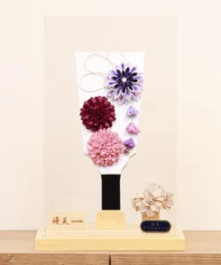 Handcrafted Hagoita paddle with purple, burgundy, and blush pink Kanzashi flowers, accented with trailing petals and displayed in a wooden base with a clear acrylic case. Wholesale by Fujiki Crafts.