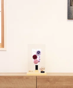 Handcrafted Hagoita paddle with purple, burgundy, and blush pink Kanzashi flowers, accented with trailing petals and displayed in a wooden base with a clear acrylic case. Wholesale by Fujiki Crafts.