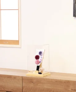 Handcrafted Hagoita paddle with purple, burgundy, and blush pink Kanzashi flowers, accented with trailing petals and displayed in a wooden base with a clear acrylic case. Wholesale by Fujiki Crafts.