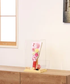 Handmade decorative Hagoita paddle adorned with soft pink, white, and yellow Kanzashi flowers, set in an acrylic case with floral handle and a red temari ball for accent. Wholesale by Fujiki Crafts.