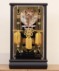Decorative Japanese Hamaya arrow display encased in glass, featuring golden tassels, black lacquered base, and symbolic arrows with feathers, used for protection and blessings. Wholesale by Fujiki Crafts.