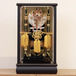 Decorative Japanese Hamaya arrow display encased in glass, featuring golden tassels, black lacquered base, and symbolic arrows with feathers, used for protection and blessings. Wholesale by Fujiki Crafts.