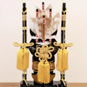 Decorative Japanese Hamaya arrow display encased in glass, featuring golden tassels, black lacquered base, and symbolic arrows with feathers, used for protection and blessings. Wholesale by Fujiki Crafts.