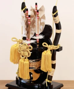 Decorative Japanese Hamaya arrow display encased in glass, featuring golden tassels, black lacquered base, and symbolic arrows with feathers, used for protection and blessings. Wholesale by Fujiki Crafts.