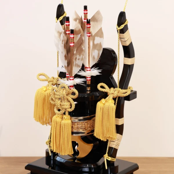 Decorative Japanese Hamaya arrow display encased in glass, featuring golden tassels, black lacquered base, and symbolic arrows with feathers, used for protection and blessings. Wholesale by Fujiki Crafts.