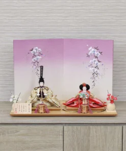 Handcrafted Japanese Hina Doll set with gold and red garments, displayed against a cherry blossom folding screen on wooden platform. Wholesale by Fujiki Crafts.