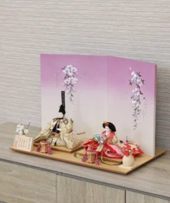 Handcrafted Japanese Hina Doll set with gold and red garments, displayed against a cherry blossom folding screen on wooden platform. Wholesale by Fujiki Crafts.