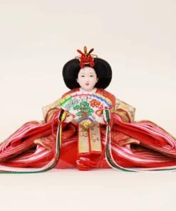 Empress Hina Doll wearing a vivid red kimono with gold detailing, holding a colorful decorative folding fan, and styled with a traditional court hairstyle topped with a red crown. Wholesale by Fujiki Crafts.