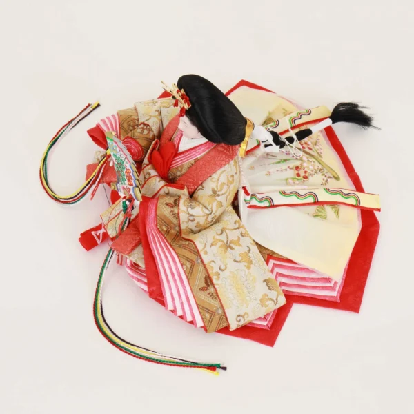 Empress Hina Doll wearing a vivid red kimono with gold detailing, holding a colorful decorative folding fan, and styled with a traditional court hairstyle topped with a red crown. Wholesale by Fujiki Crafts.