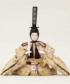 Emperor Hina Doll dressed in a pale gold brocade kimono with intricate patterns, holding a slender fan and wearing a tall black traditional court headdress. Wholesale by Fujiki Crafts.