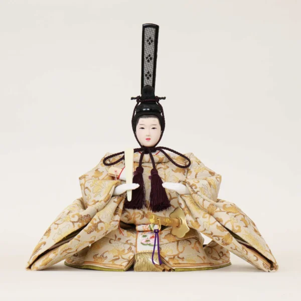 Emperor Hina Doll dressed in a pale gold brocade kimono with intricate patterns, holding a slender fan and wearing a tall black traditional court headdress. Wholesale by Fujiki Crafts.