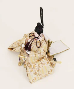 Emperor Hina Doll dressed in a pale gold brocade kimono with intricate patterns, holding a slender fan and wearing a tall black traditional court headdress. Wholesale by Fujiki Crafts.