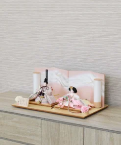 Elegant Hina doll set featuring pastel-striped Emperor and soft pink Empress dolls seated before a gradient peach folding screen, flanked by cylindrical lanterns and floral accents on a wooden display base. Wholesale by Fujiki Crafts.