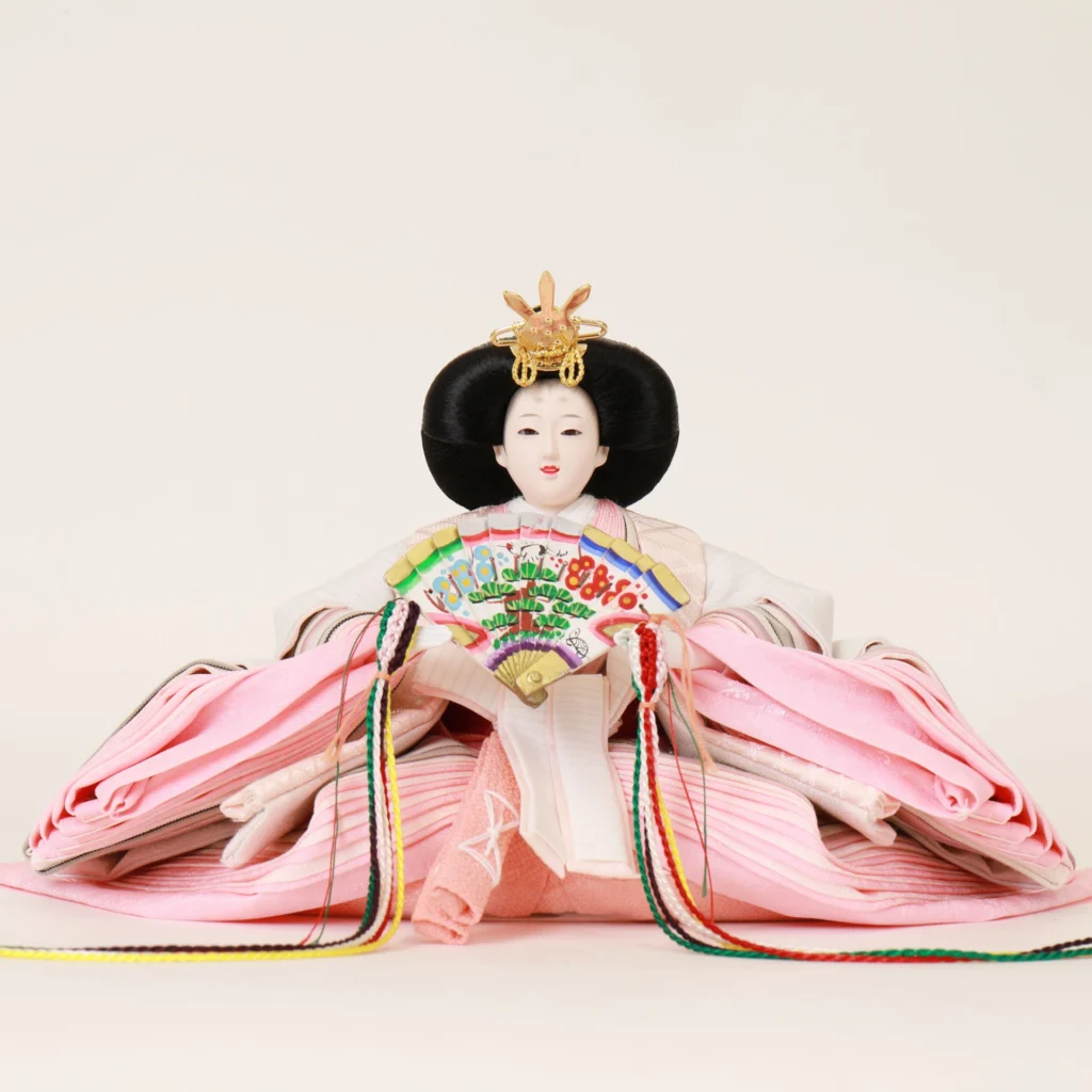 Close-up of traditional Japanese Empress Hina Doll in layered pink kimono, holding a colorful fan with gold and red kanzashi crown on a white background. Wholesale by Fujiki Crafts.